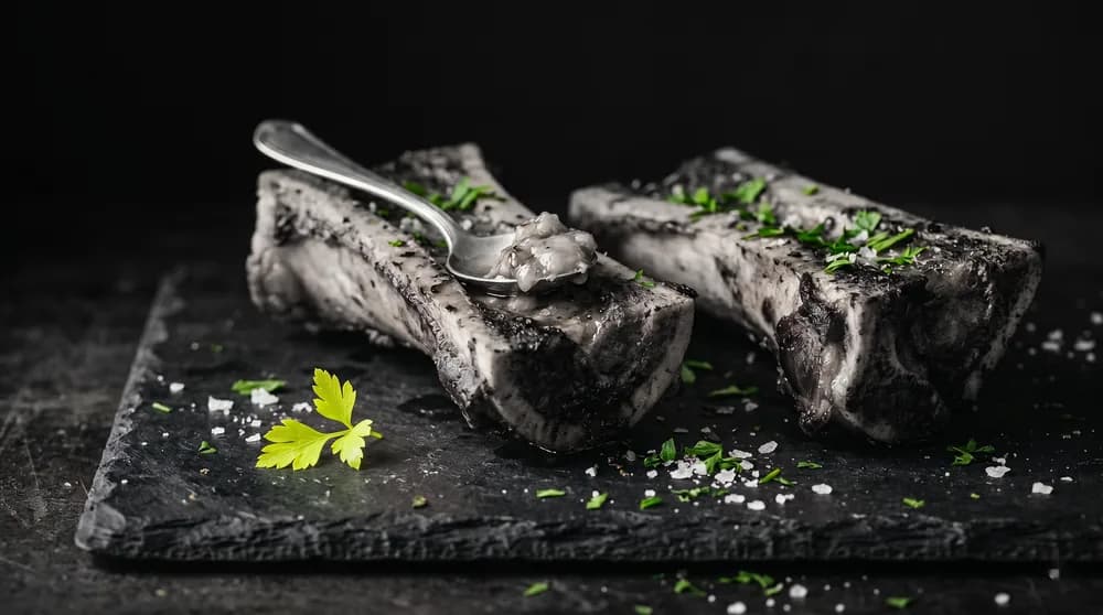 Längs halbierte Markknochen mit Löffel, grobem Meersalz und Petersilie auf dunklem Schieferbrett