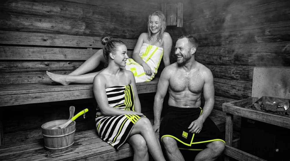 Entspannte Menschen in einer finnischen Holzsauna mit Aufguss-Kübel und heißen Steinen — regelmäßige Hitze als kardiovaskulärer Longevity-Hebel